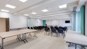 Un salón de conferencias con una larga mesa, sillas, una pizarra y una pantalla para proyector.