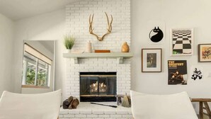 A living room with a white brick fireplace, a mounted deer head, and a checkered wall art piece.