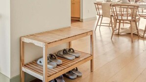 A modern interior with a wooden bench holding shoes, a dining area with wooden chairs, and a wall with wooden wall art.