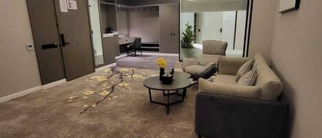 A modern living room with a sofa, armchair, and coffee table. There is a door leading to a kitchen area.