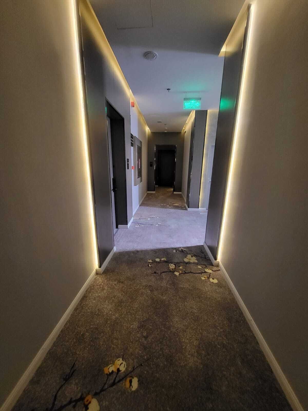 Un pasillo de hotel con pisos alfombrados, paredes y un respiradero en el techo.