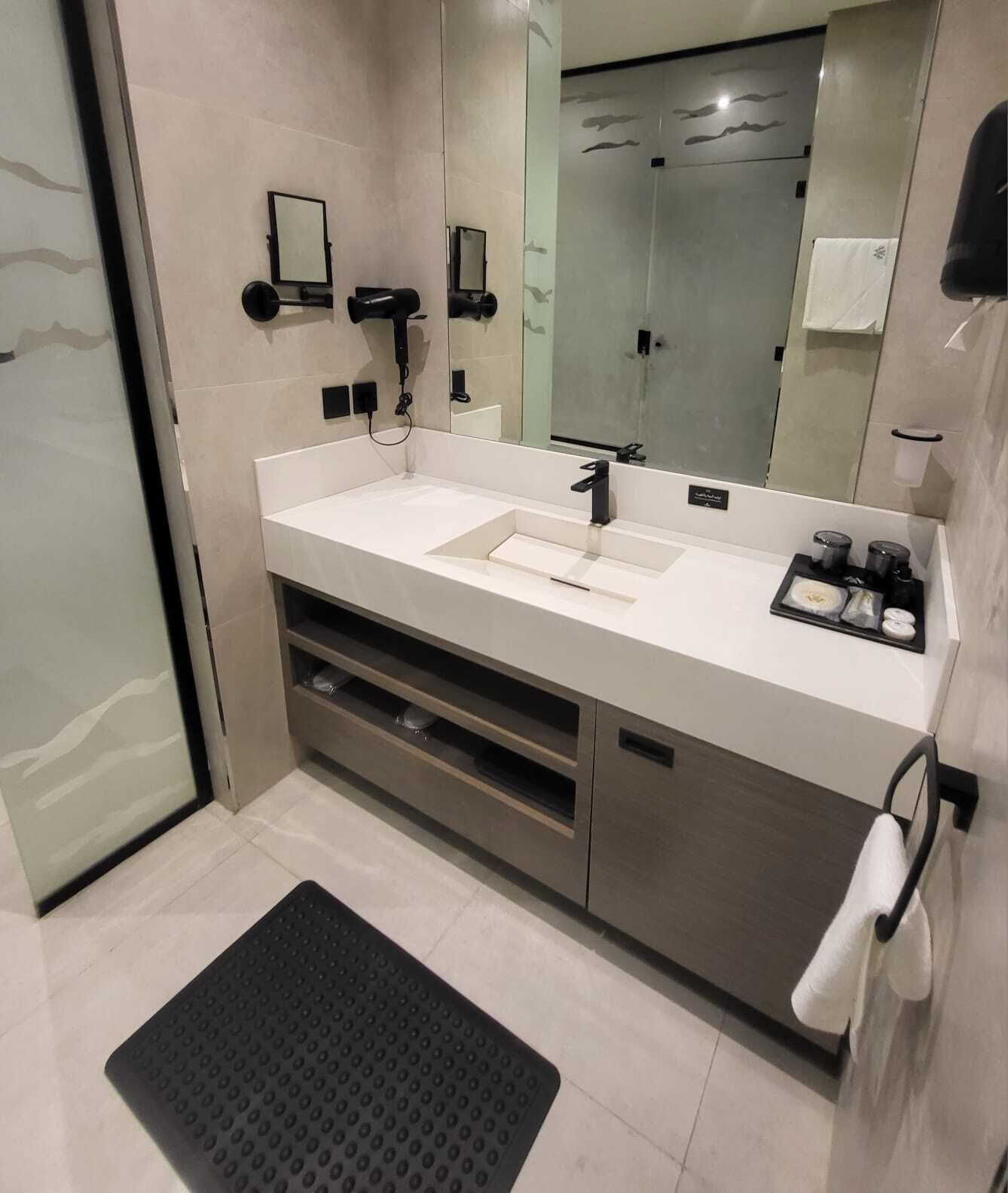 A modern bathroom with a large mirror, two sinks, a towel rack, and a shower area.