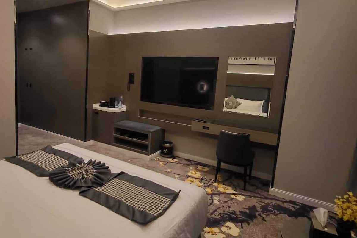 A modern hotel room with a large bed, a flat-screen TV, a desk, and a seating area.