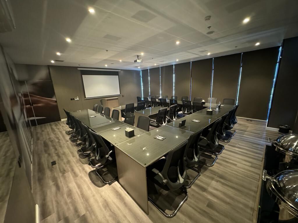 Une salle de conférence avec une longue table, des chaises, un écran de projection et une grande fenêtre.