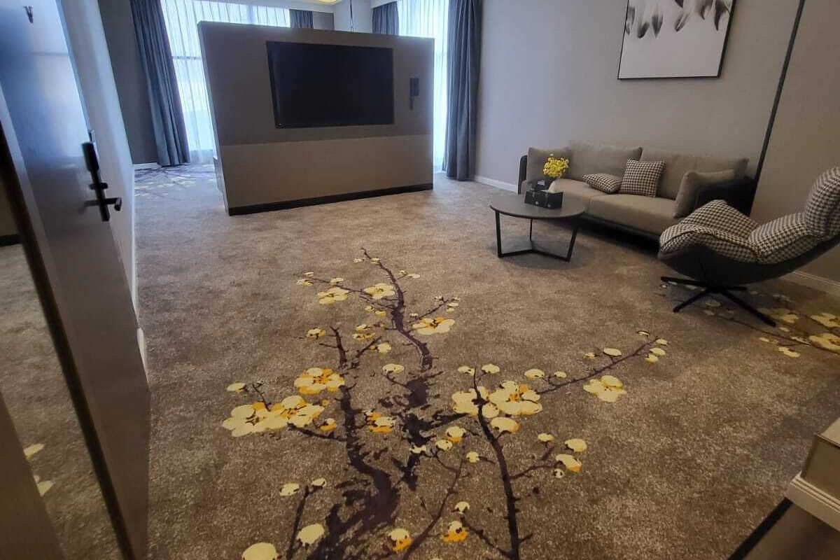 A modern living room with a large flat-screen TV, a sofa, a coffee table, and a patterned carpet.
