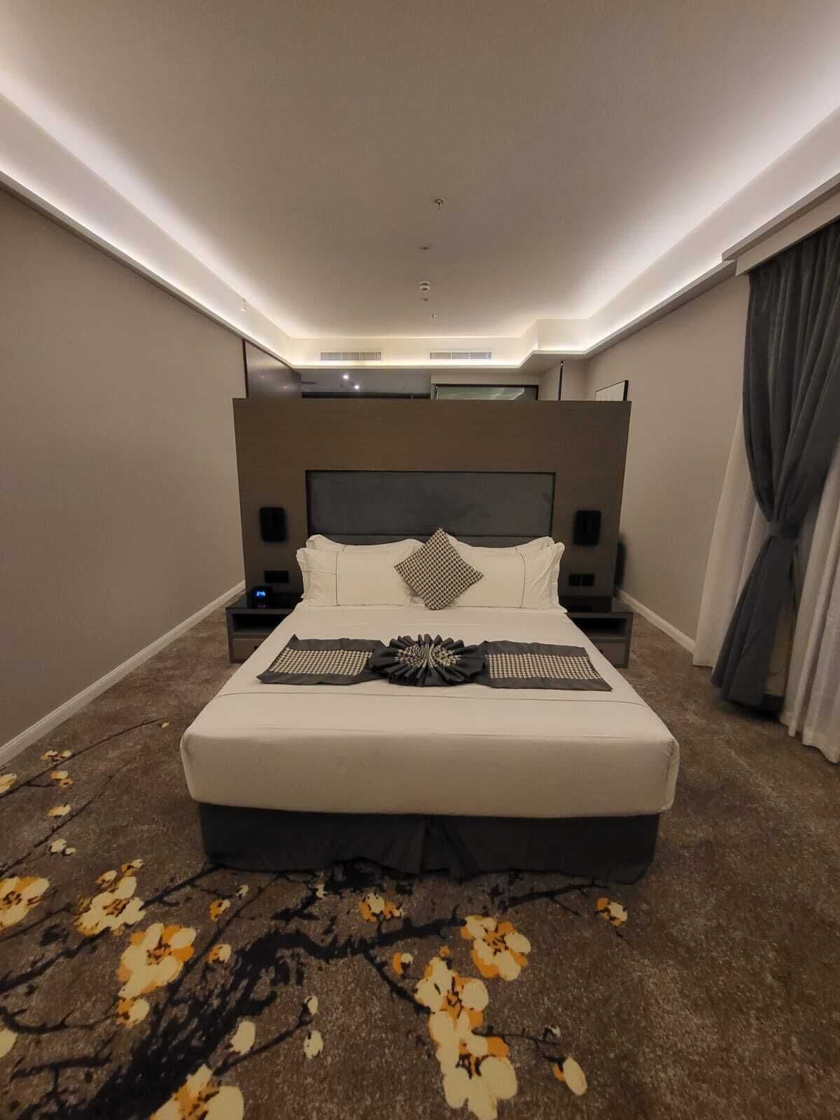 A modern hotel room with a large bed, bedside tables, and a ceiling light.