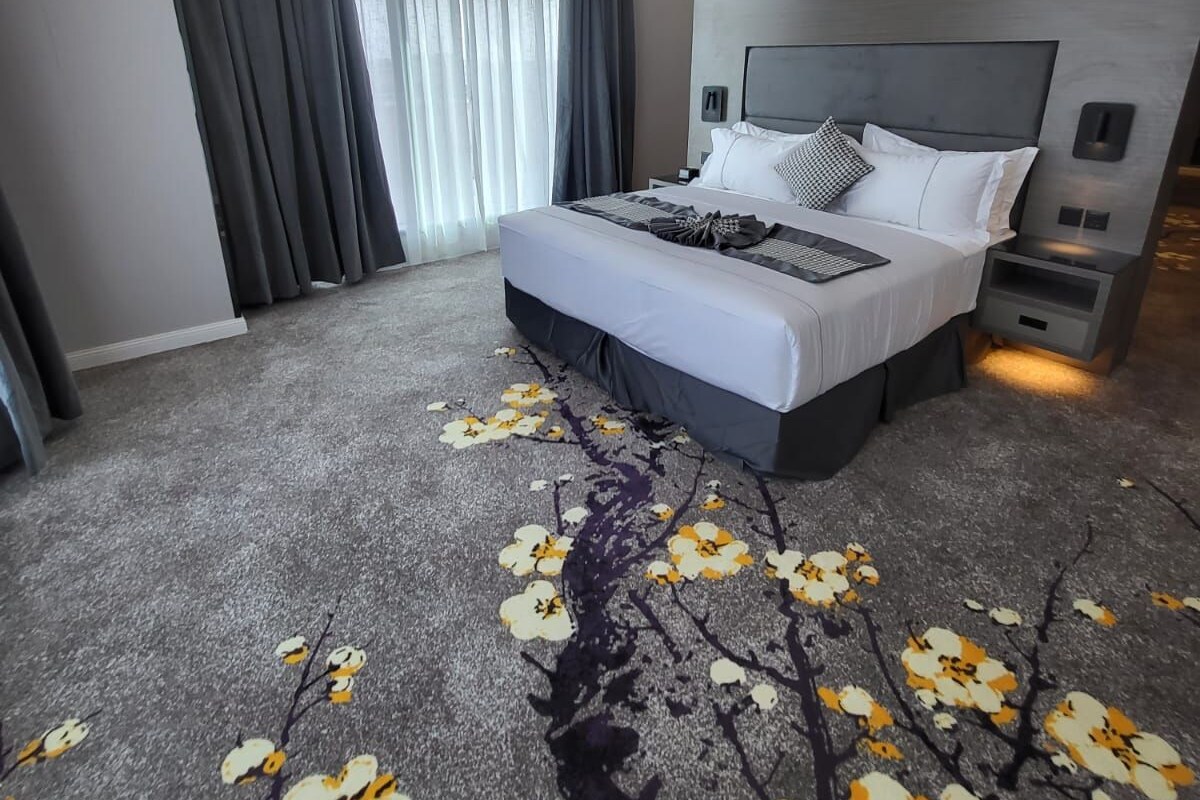 A modern hotel room with a large bed, a nightstand, a built-in TV, and a window with curtains.