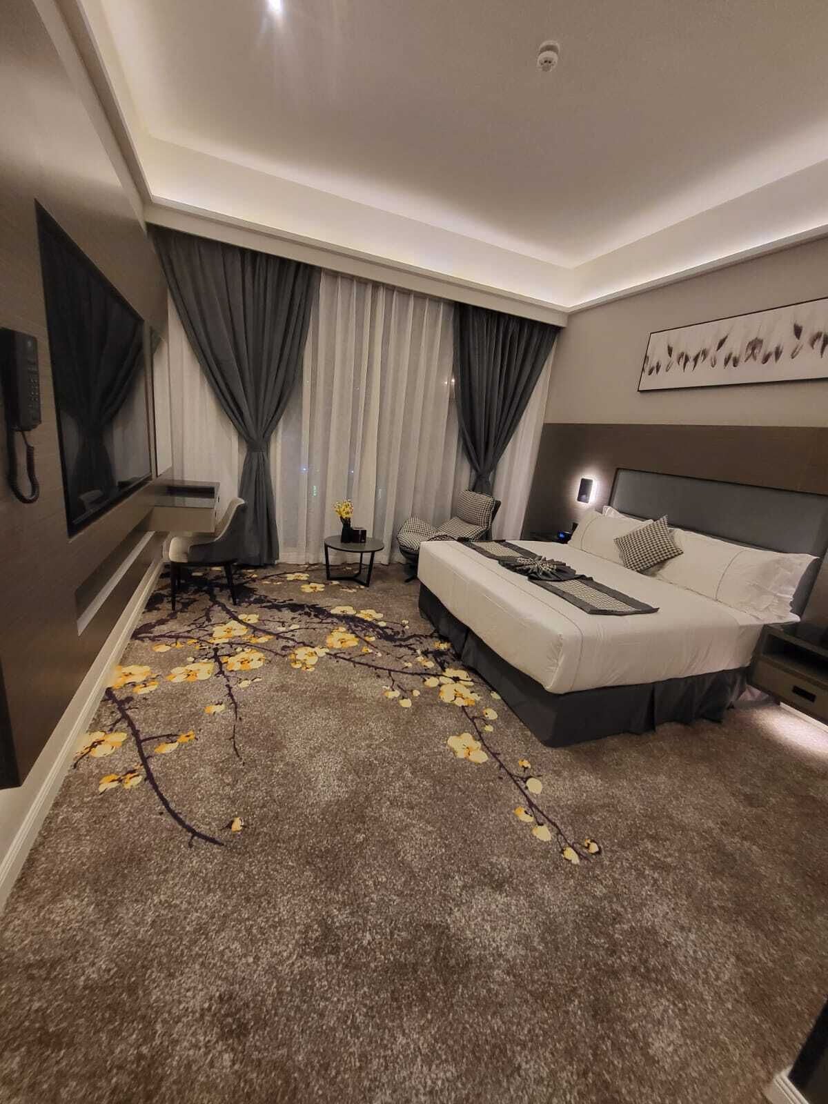 A modern hotel room with a large bed, a desk, a chair, and a small table.