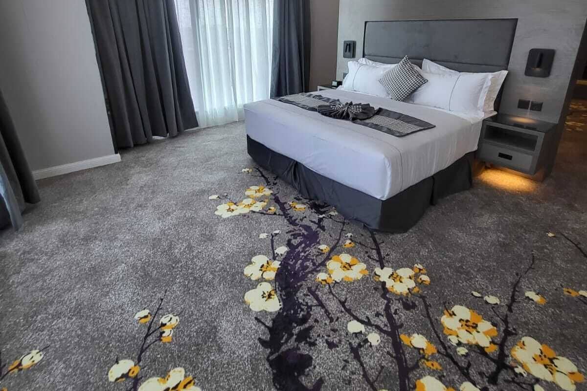 A modern hotel room with a large bed, a nightstand, a built-in TV, and a window with curtains.