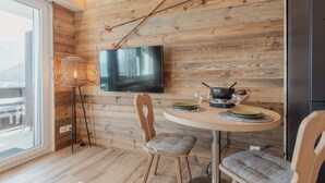 Ein Zimmer mit Holzwänden, einem an der Wand befestigten Fernseher, einem Esstisch mit Stühlen und einem Fenster mit Aussicht.