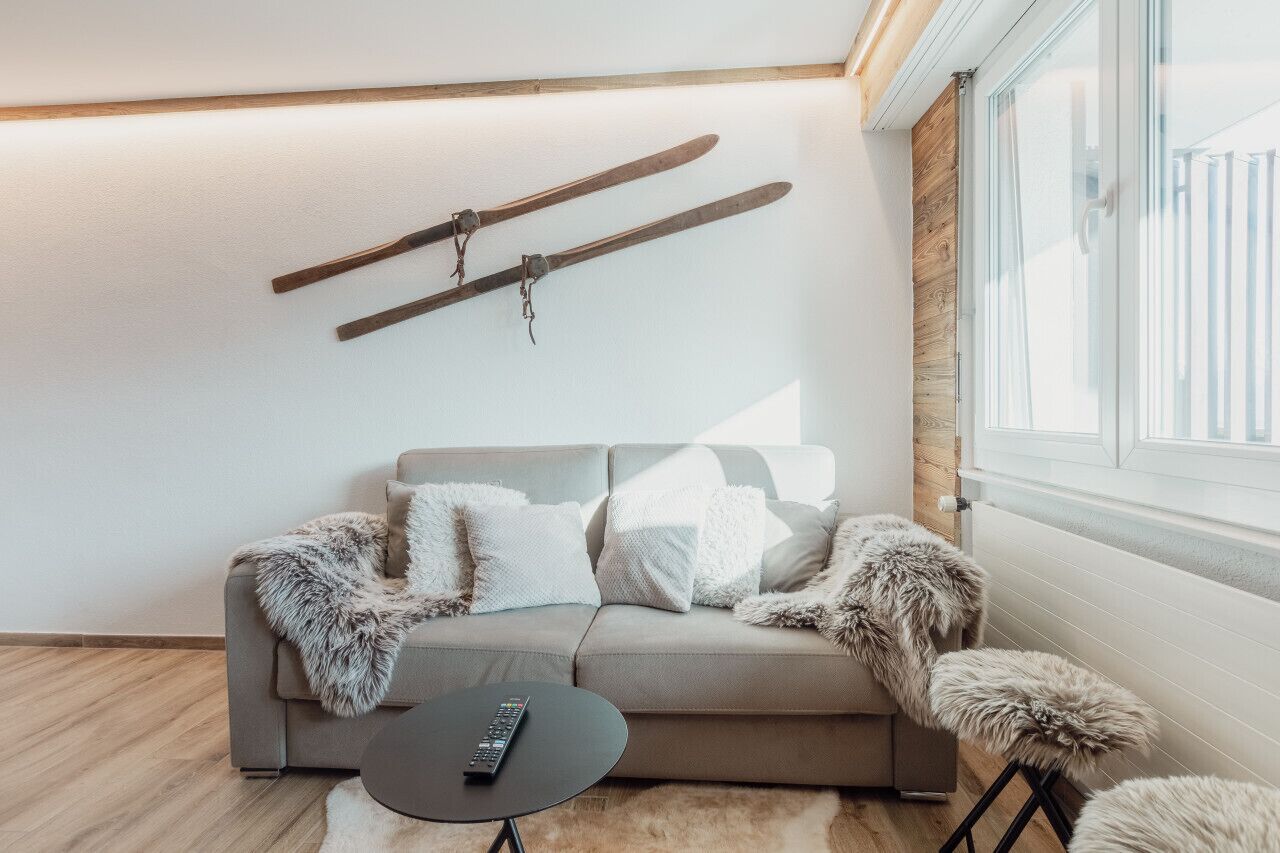 A modern living room with a sofa, a remote control on a small table, and a pair of skis hanging on the wall.
