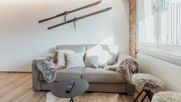 A modern living room with a sofa, a remote control on a small table, and a pair of skis hanging on the wall. - Charmant Studio Avec une vue Imprenable (Nendaz)