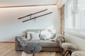 A modern living room with a sofa, fluffy throw pillows, a remote control on a small table, and wooden skis mounted on the wall. - Charmant Studio Avec une vue Imprenable (Nendaz)