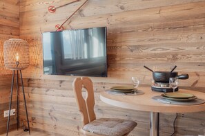 A wooden interior with a round dining table, a TV mounted on the wall, a chair, and a table lamp. - Charmant Studio Avec une vue Imprenable (Nendaz)