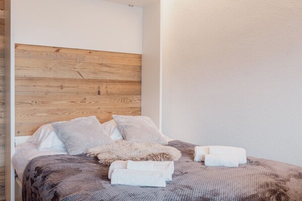 A neatly made bed with a wooden headboard, white and gray bedding, and a fluffy throw.