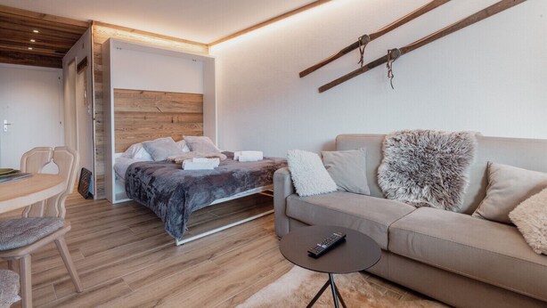 Ein modernes Schlafzimmer mit einem Bett, einem Schlafsofa, einem Esstisch und einer Fernbedienung auf einem kleinen Tisch.