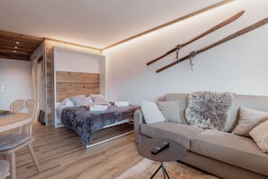 A modern bedroom with a bed, a sofa, a small table, and a ski rack on the wall.