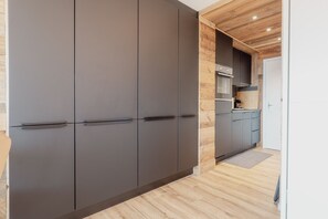 A modern kitchen with dark cabinets, wooden flooring, and a built-in oven. - Charmant Studio Avec une vue Imprenable (Nendaz)