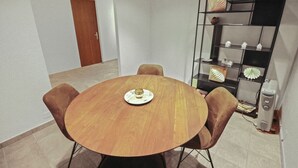 A room with a round wooden table, four chairs, a bookshelf with decorative items, and a door in the background. - Charmant Studio Ouvert Avec vue Paisible (Crans-Montana)