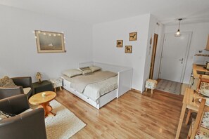 Un dormitorio con cama, una mesita, una silla y un sofá. Hay una puerta y una ventana en la habitación.