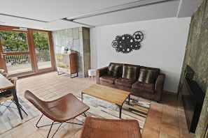 Un salon avec un canapé en cuir marron, une table basse en bois, des fauteuils en osier et un élément décoratif mural.