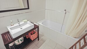A bathroom with a white sink, mirror, and bathtub. - Charmant Studio Ouvert Avec vue Paisible (Crans-Montana)
