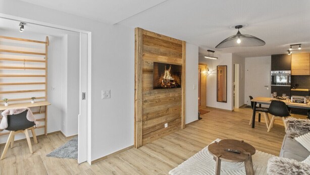 A modern living room with a wooden accent wall, a fireplace, a dining area, and a kitchen. - Appartement rénové avec vue panoramique et sauna (Saas-Fee)