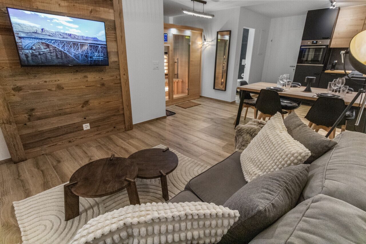 Ein modernes Wohnzimmer mit einer Wandvertäfelung aus Holz, einem Flachbildfernseher, einem Essbereich mit Holztisch und -stühlen sowie einer Küchenzeile mit Herd und Kühlschrank.