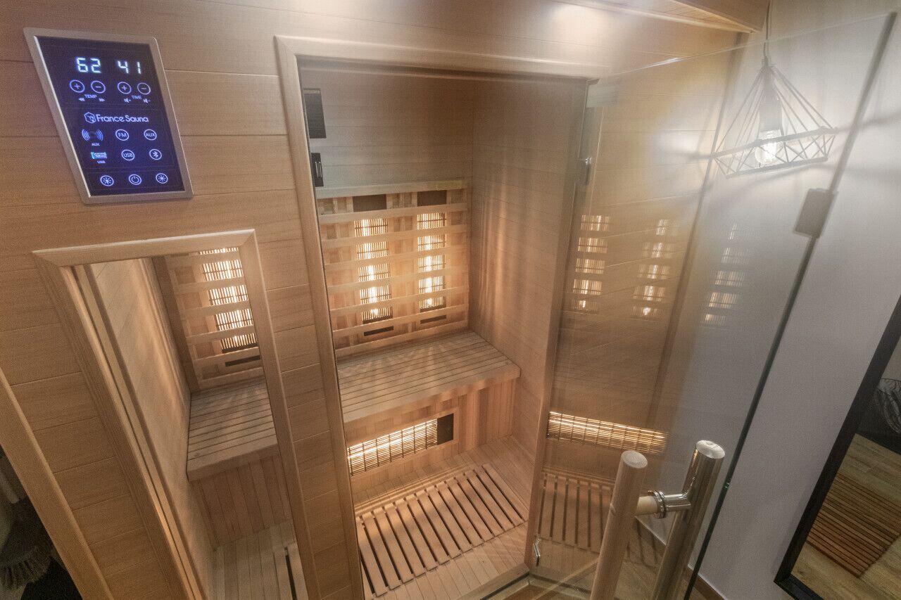 Uma sauna com painel digital, bancos de madeira e porta de vidro.
