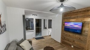 A modern living room with a grey sofa, a small wooden table, and a TV on a wooden wall. - Appartement rénové avec vue panoramique et sauna (Saas-Fee)