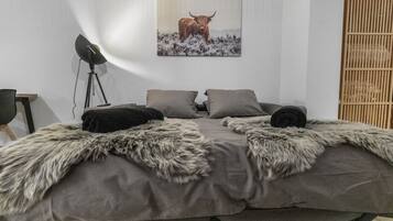 Een slaapkamer met een bed, twee kussens, een bont plaid, een staande lamp en een ingelijste foto aan de muur.