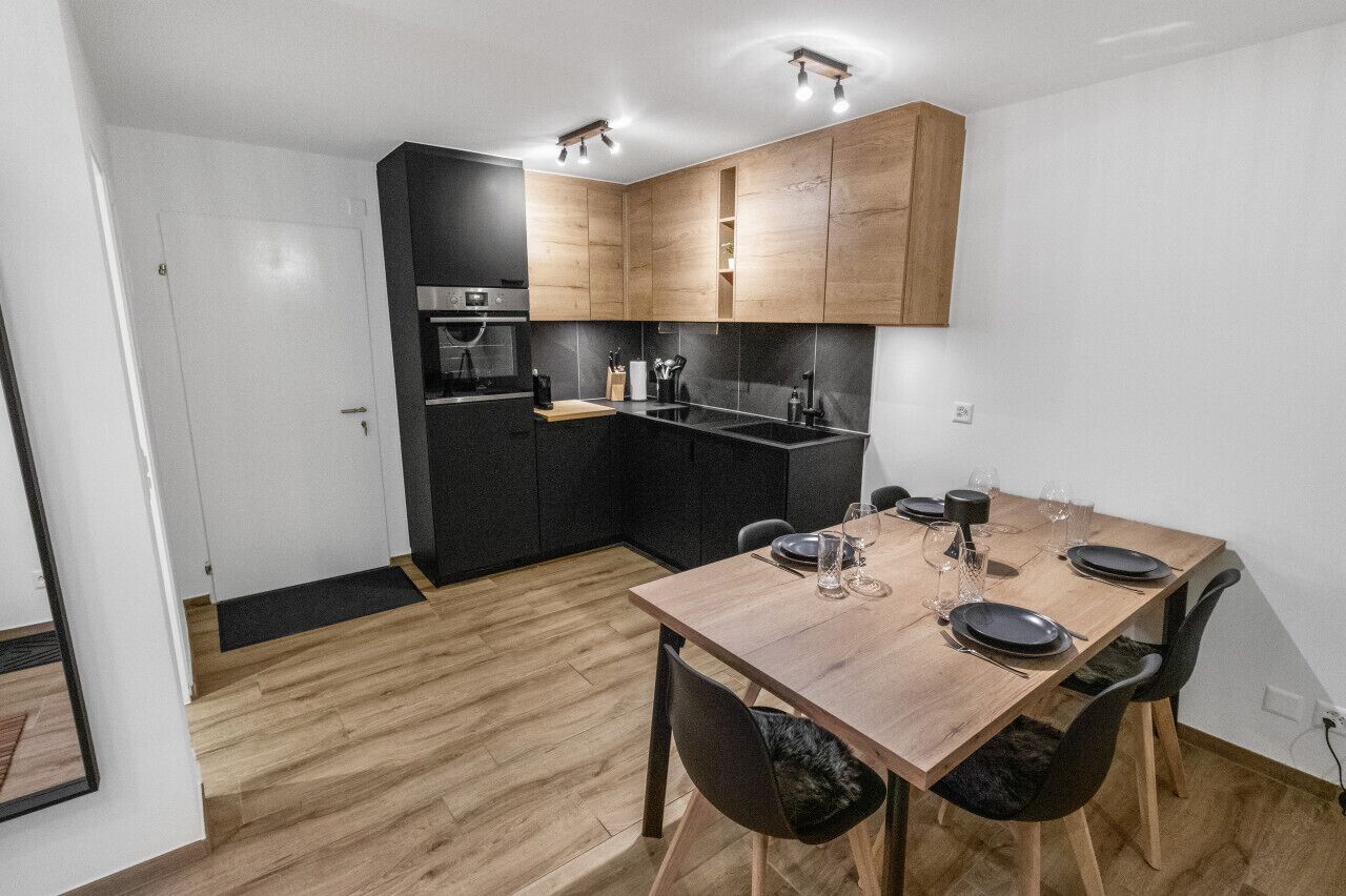 A modern kitchen with wooden cabinets, a built-in oven, and a dining area with a wooden table and chairs.