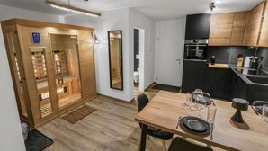 A modern kitchen with wooden cabinets, a built-in oven, and a dining area with a wooden table set for two. - Appartement rénové avec vue panoramique et sauna (Saas-Fee)