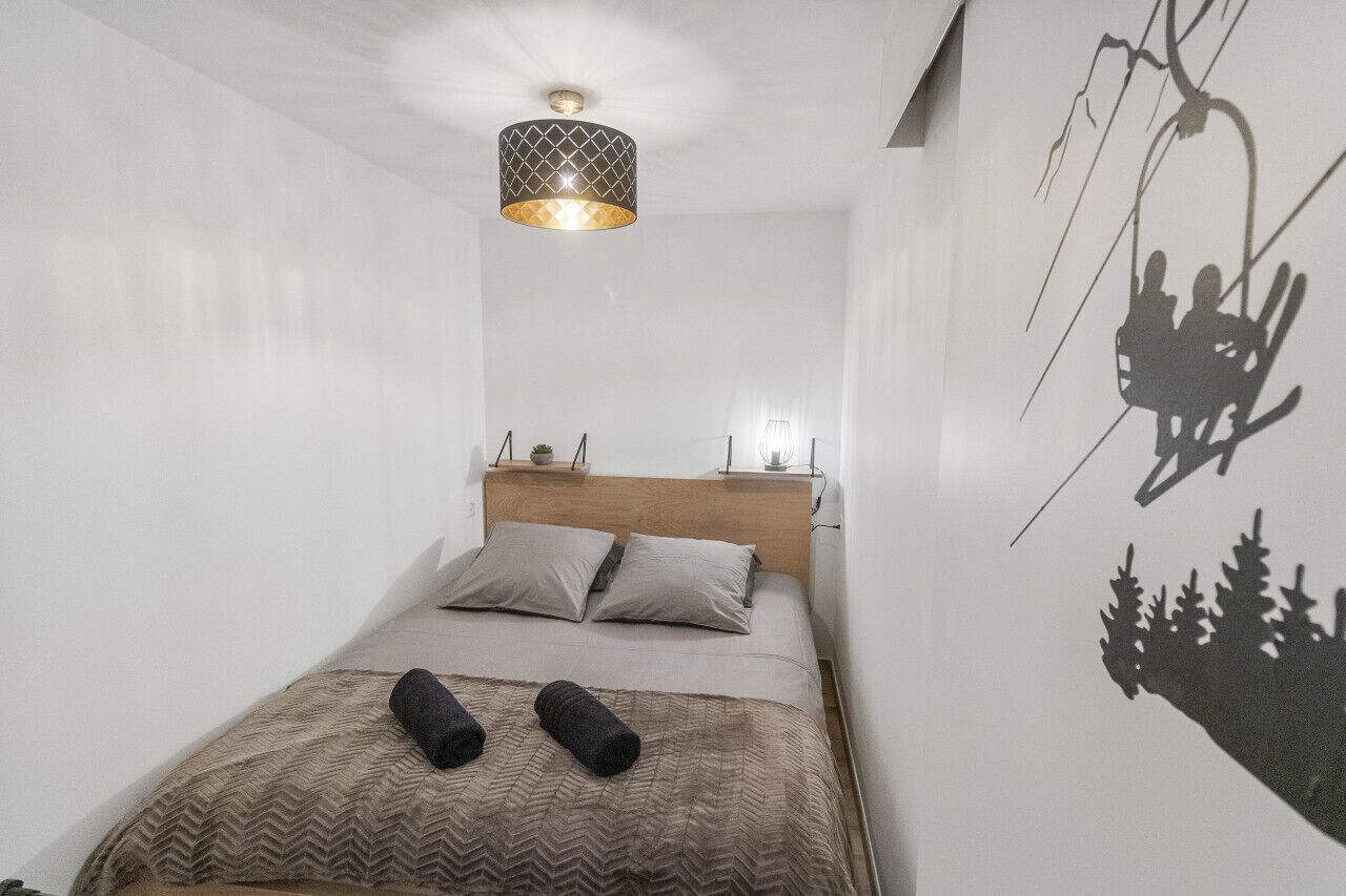 Un dormitorio con cama, cabecera, mesita de noche, lámpara y una obra de arte en la pared que representa un paisaje montañoso.