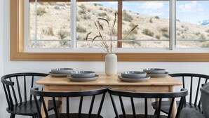 Une table à manger avec six bols gris et un vase blanc contenant des plantes séchées, le tout placé devant une fenêtre donnant sur un paysage désertique.
