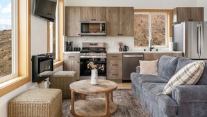 Une cuisine moderne avec des meubles en bois, un four à micro-ondes, une cuisinière et un réfrigérateur. On y trouve un canapé gris et une table ronde en bois sur laquelle est posé un vase.