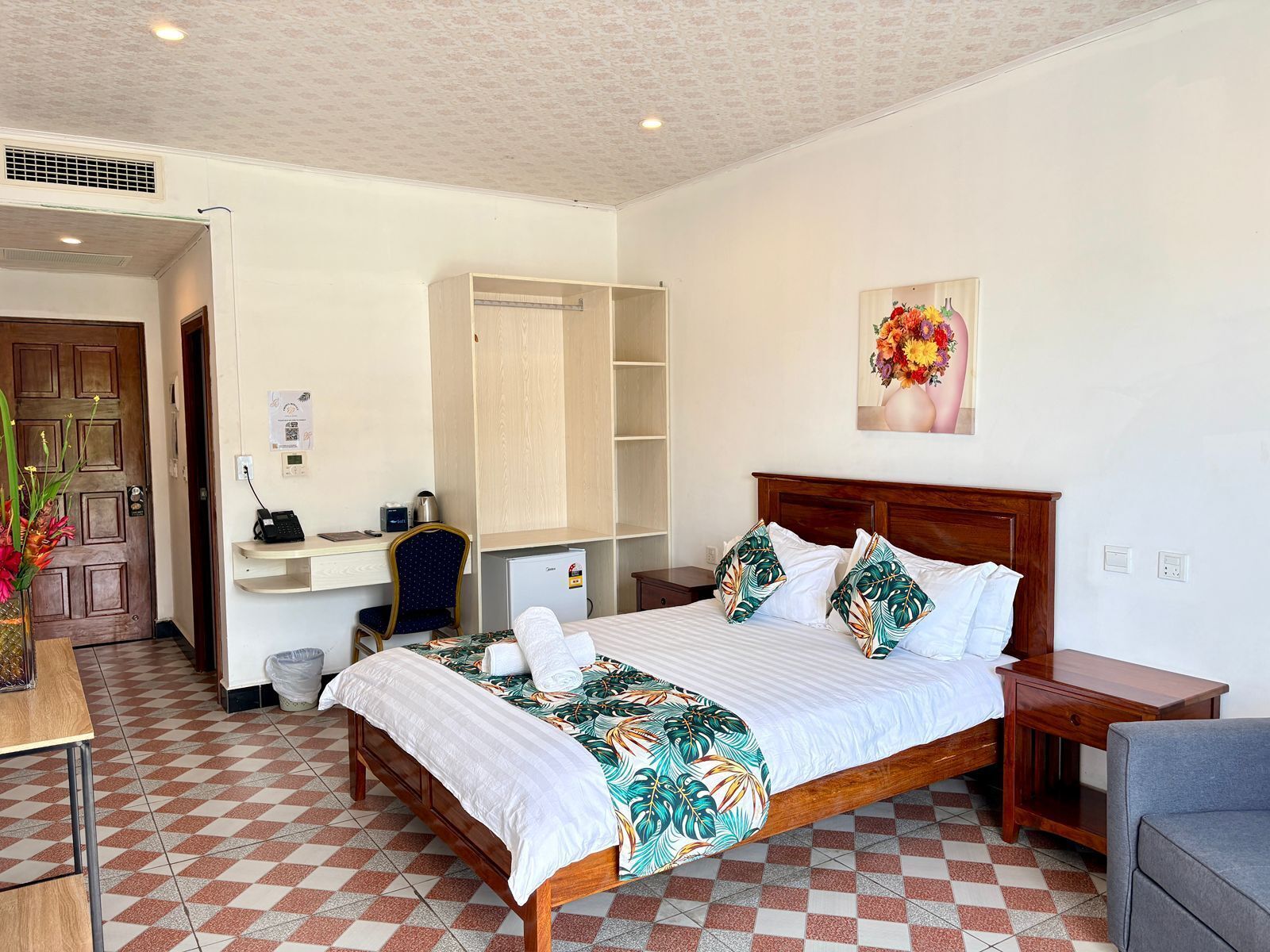 Une chambre d’hôtel équipée d’un lit, d’un bureau, d’une chaise, d’une petite table et d’une étagère fixée au mur.