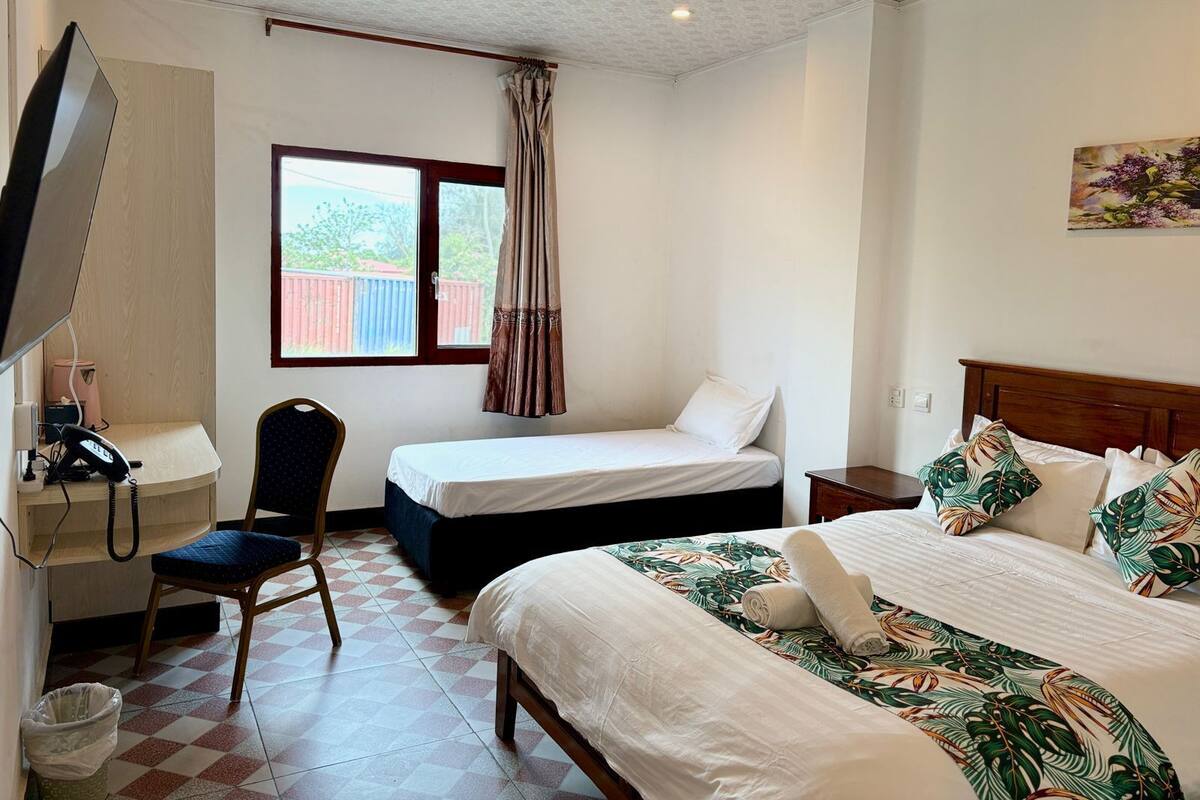 Habitación de hotel con cama, escritorio con teléfono, una silla, ventana con cortinas y un cuadro en la pared.