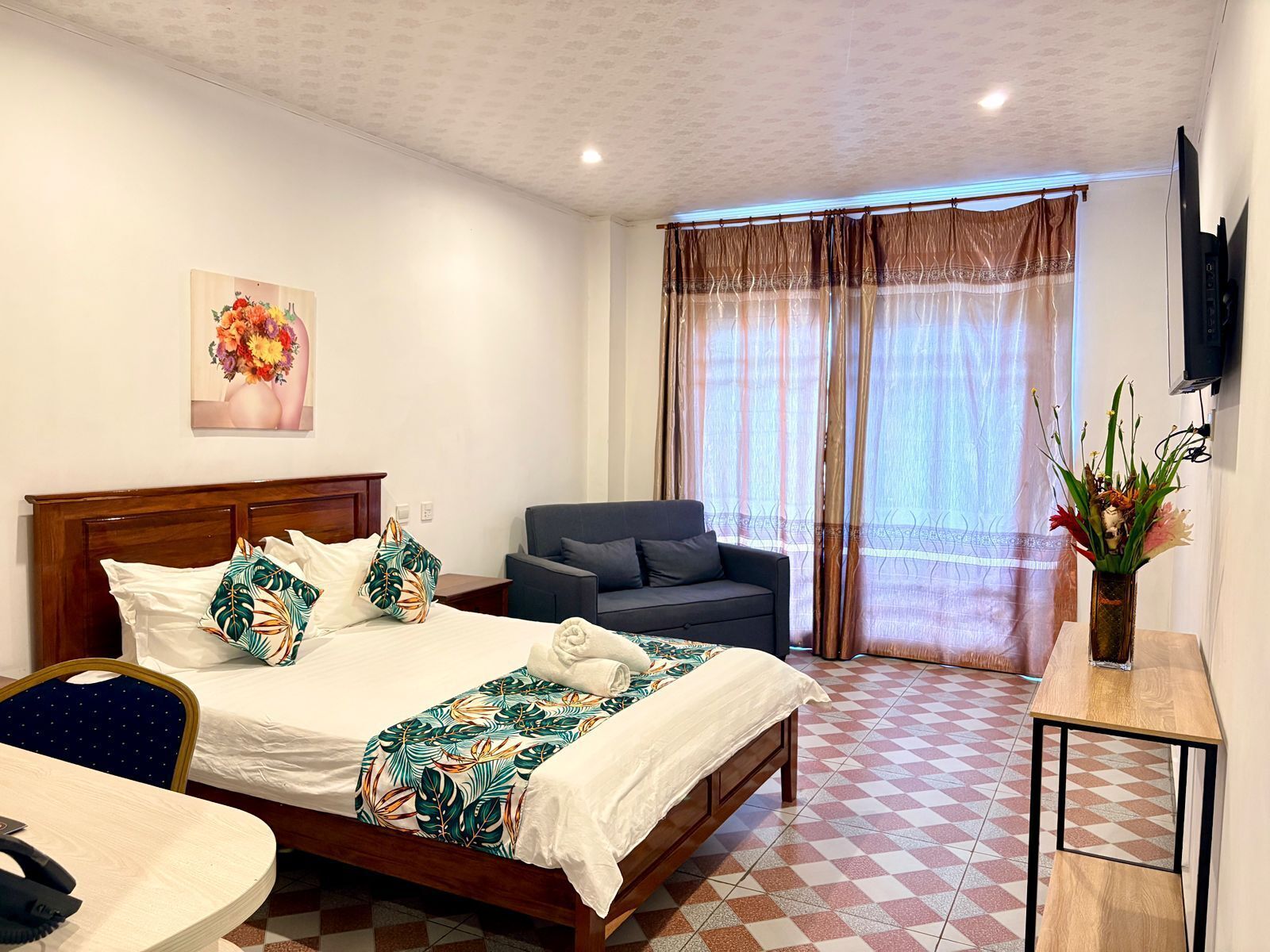 A hotel room with a bed, a chair, a desk, a TV, and a window with curtains.