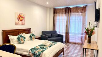 A hotel room with a bed, a chair, a desk, a TV, and a window with curtains.