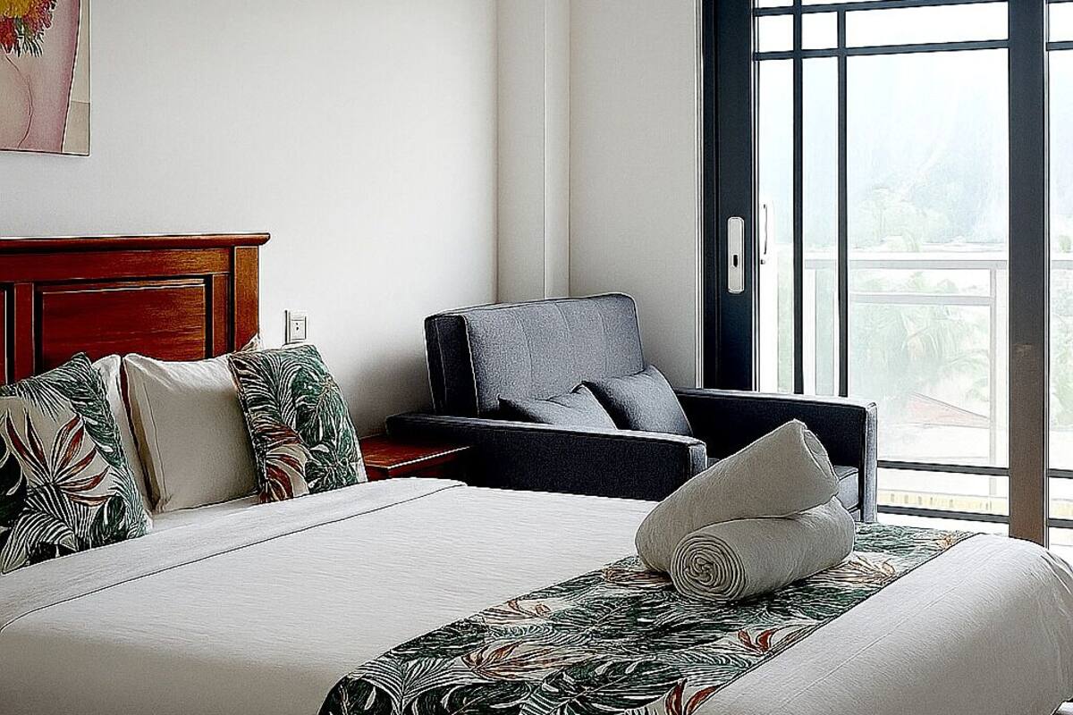Un dormitorio con una cama grande, una silla, una mesita de noche y una ventana con vistas.