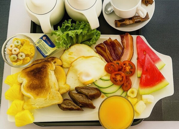 A breakfast tray with toast, eggs, bacon, tomatoes, cucumber slices, watermelon, and a glass of orange juice.