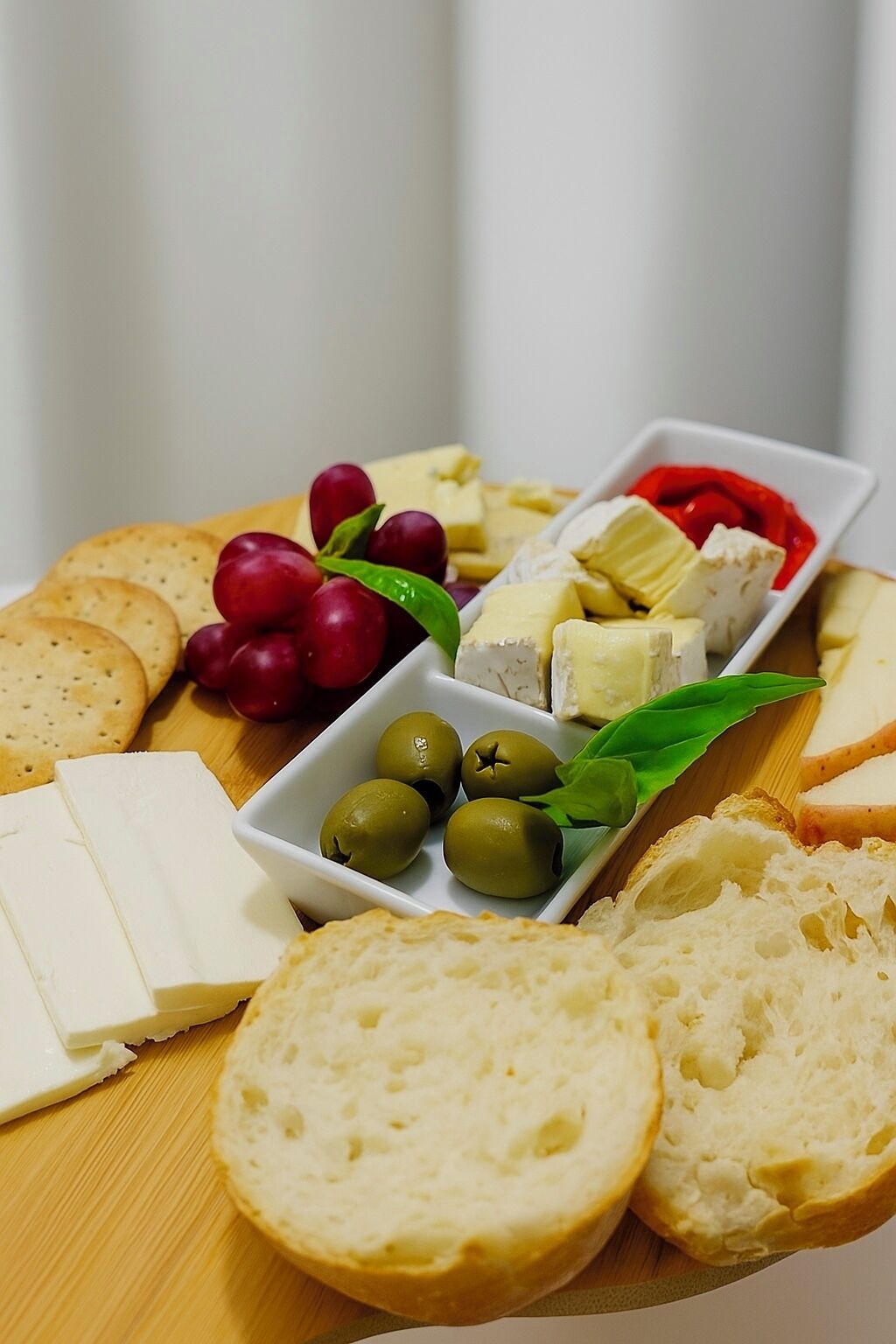A charcuterie board with various cheeses, grapes, olives, crackers, and bread.