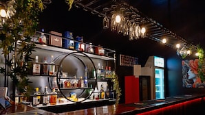 Un espace bar avec des étagères remplies de bouteilles d’alcool, un comptoir circulaire et des luminaires suspendus.