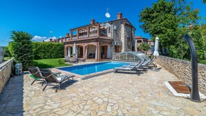 Une villa dotée d’une piscine, de chaises longues et d’une terrasse en pierre.