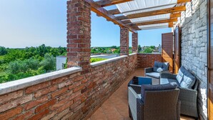 Un balcon abrité avec des murs en briques, une pergola en bois et des meubles en osier.