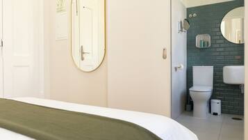 Ett hotellrum med en säng, en spegel, en dörr och utsikt in i badrummet.