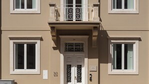 Un immeuble à plusieurs étages doté d’une façade symétrique, avec une entrée centrale flanquée d’une double porte et un balcon orné de balustrades décoratives.