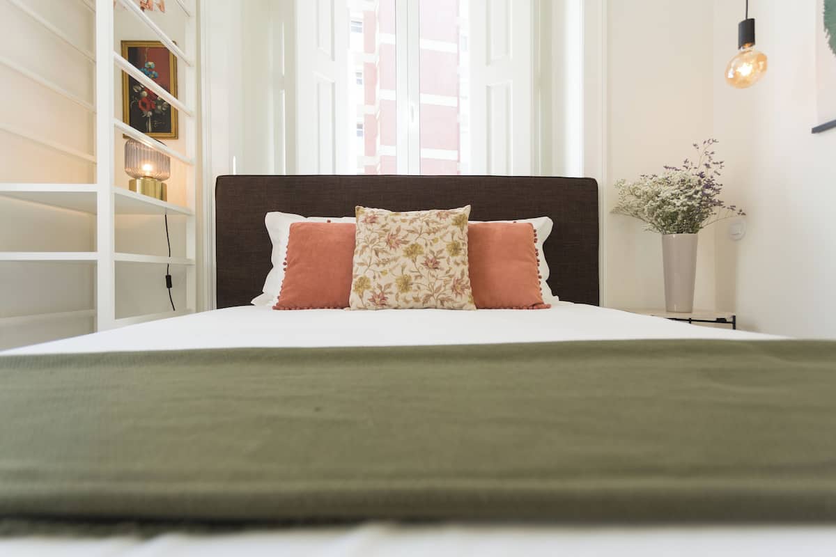 A neatly made bed with a green throw blanket, two pillows, and a headboard.