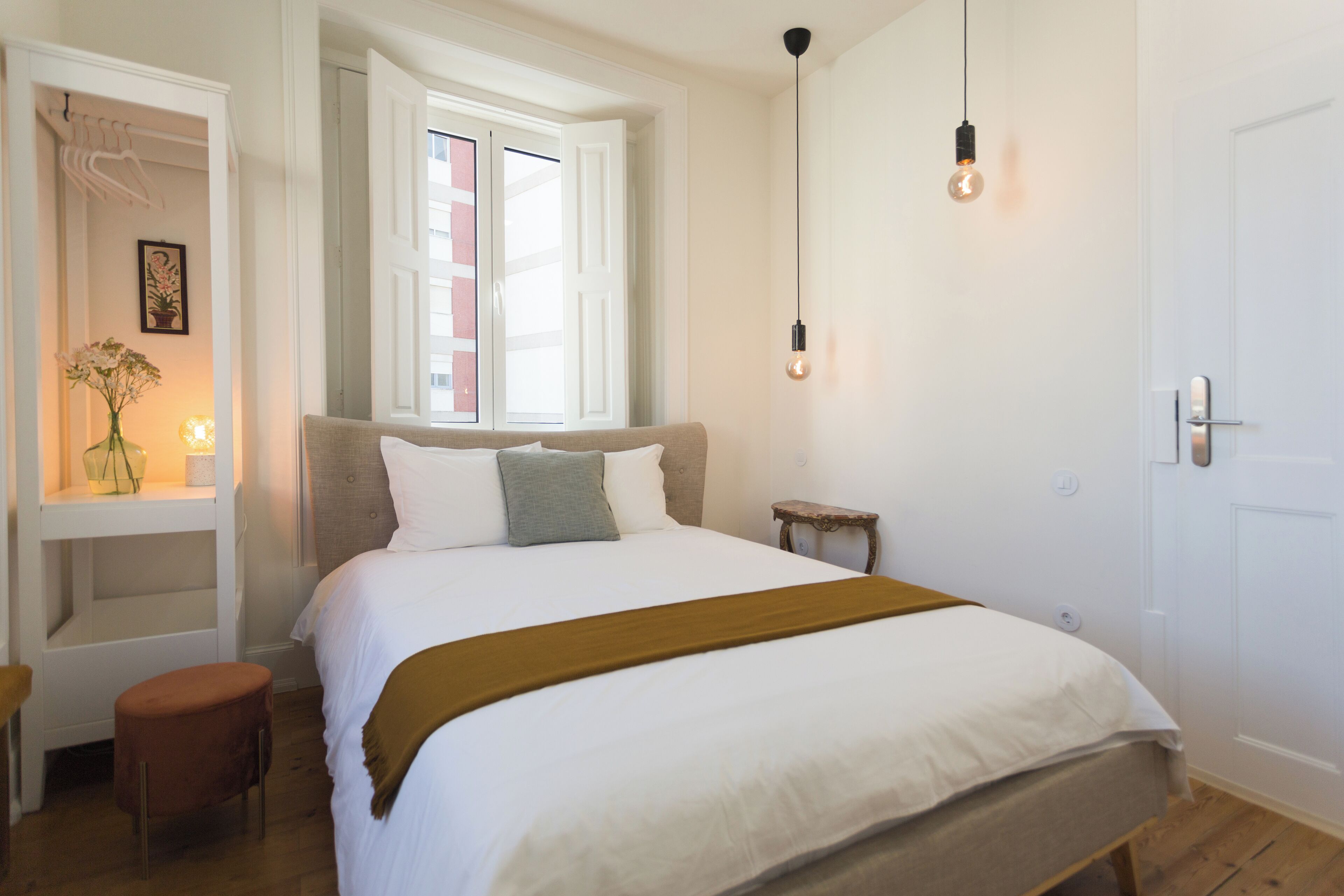 A bedroom with a bed, a bedside table, a nightstand, a window, and a door.
